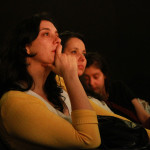 Foto ilustrando á reação de duas mulheres assistindo uma palestra , onde a segunda mulher ao centro da foto tem uma menina dormindo ao seu colo.