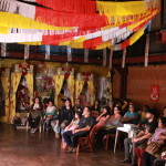 Foto mostrando pessoas assistindo algo em um telão.