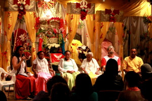 Foto ilustrando um diálogo entre pessoas, composto por quatro mulheres e dois homens, onde todos estão em um palco falando ao público.