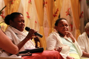 Foto ilustrando um diálogo entre pessoas, onde há  duas mulheres negras na imagem , onde a mulher da esquerda tem as mãos um microfone.