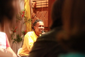 Foto ilustrando um diálogo entre pessoas , onde ao centro da imagem há um homem negro com um microfone na mão.