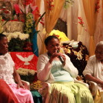 Imagem ilustrando um diálogo entre pessoas , ao centro da imagem há uma mulher negra com um microfone na mão , á esquerda há uma mulher e ao lado direito á uma senhora .