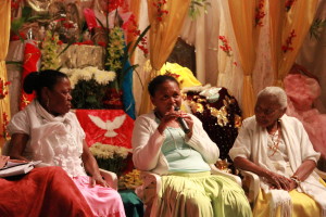 Imagem ilustrando um diálogo entre pessoas , ao centro da imagem há uma mulher negra com um microfone na mão , á esquerda há uma mulher  e ao lado direito á uma senhora .