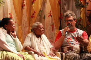 Imagem ilustrando um diálogo entre três pessoas  , uma senhora e uma mulher negra  á esquerdada imagem e um homem á direita com um microfone na mão.