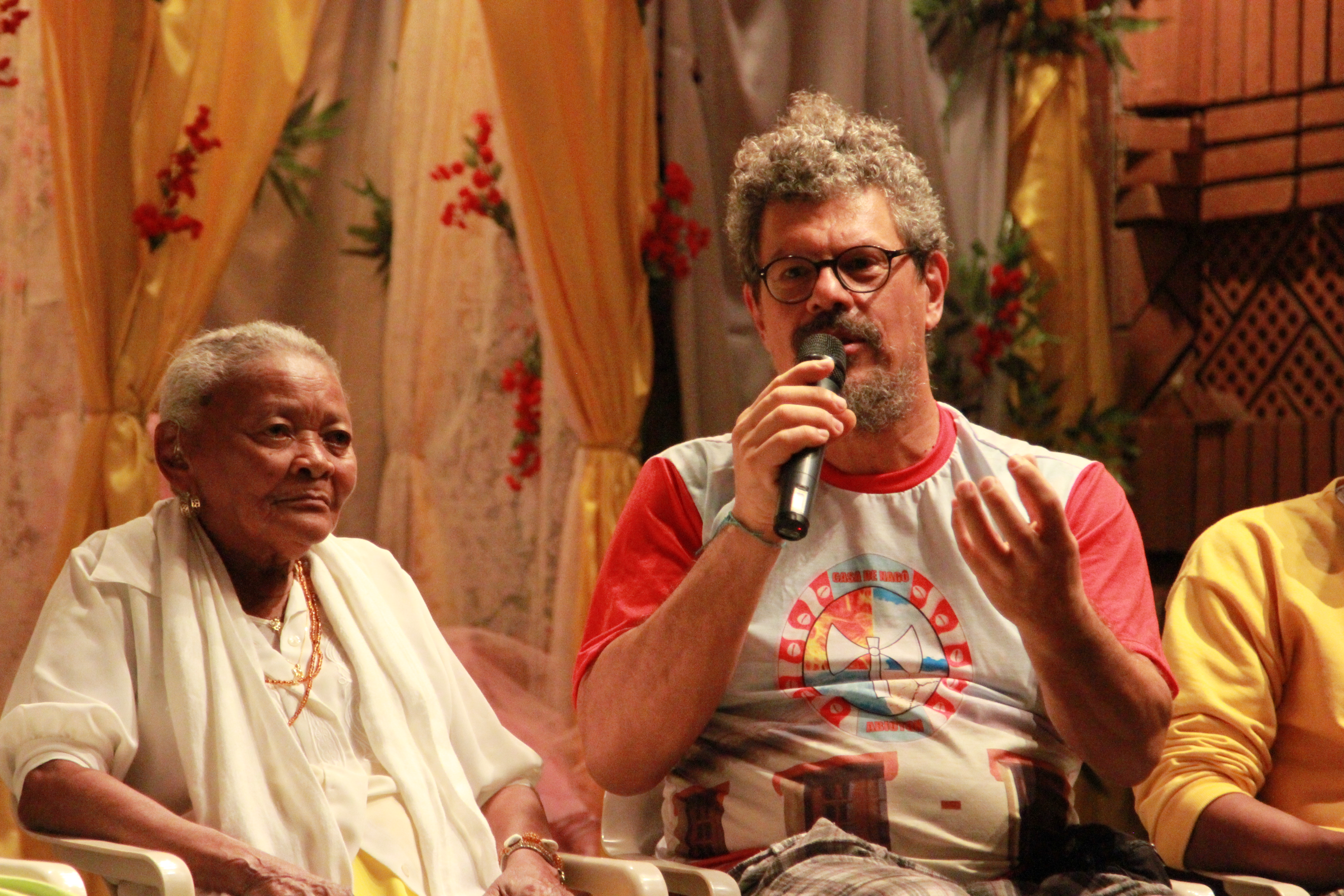 Imagem ilustrando um diálogo de duas pessoas , uma senhora negra á esquerda e um homem á direita com um microfone na mão.