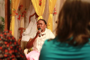 Imagem ilustrando um diálogo onde há uma mulher negra com um microfone falando a um grupo de pessoas.