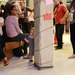 Foto ilustrando interação entre pessoas , onde á um pilar ao centro da imagem onde se encontra uma criança por trás do pilar sorrindo.