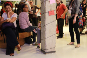 Foto ilustrando interação entre pessoas , onde á um pilar ao centro da imagem onde se encontra uma criança por trás do pilar sorrindo.