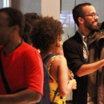 Foto ilustrando interação entre pessoas , á esquerda á um homem negro , ao centro uma mulher negra e á direita um outro homem.