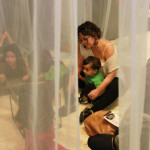 Foto com quatro crianças se interagindo , onde ao centro á uma mulher com um menino sentado em seu colo.