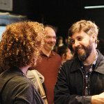 Foto ilustrando interação entre pessoas , onde ao centro á um homem e uma mulher tendo um diálogo e sorrindo.