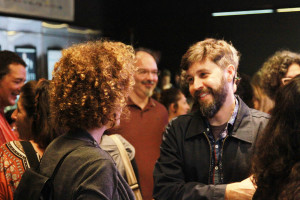Foto ilustrando interação entre pessoas , onde ao centro á um homem e uma mulher tendo um diálogo e sorrindo.