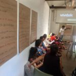 Foto de um home apontando para um quando enquanto uma turma de pessoas o observa.