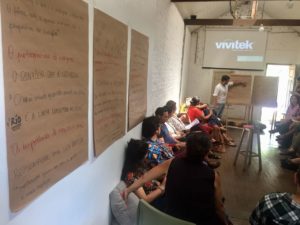 Foto de um home apontando para um quando enquanto uma turma de pessoas o observa.