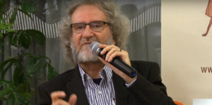 Homem Grisalho falando ao microfone.